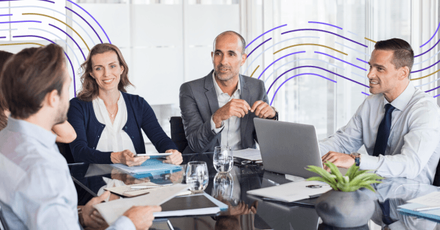 Professional team of five business executives collaborating at modern conference table with laptops and documents during c...