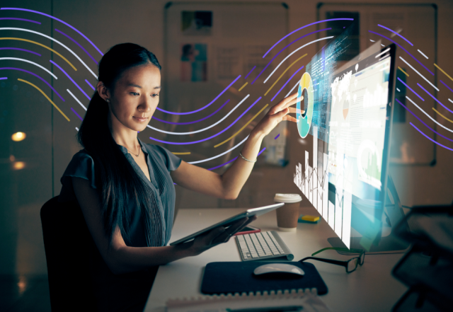 Professional woman analyzing digital data visualization on computer monitor with colorful wave graphics in modern office w...